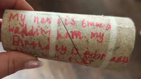A person holding a carboard toilet roll tube bearing a child's handwritten message in red felt tip