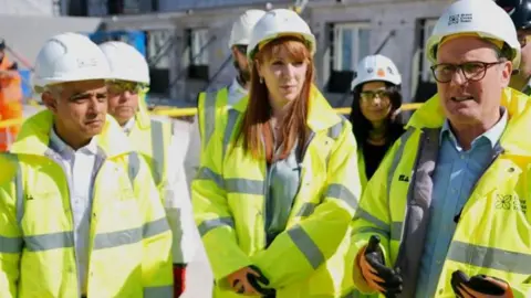 PA Media Sadiq Khan, Angela Rayner and Sir Keir Starmer wearing hi-vis jackets and achromatic  hard   hats connected  a gathering  site