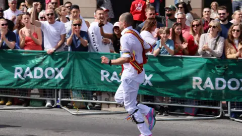 Kevin Boorman A man wearing a Morris dancing costume while running a marathon as the crowd cheers him on