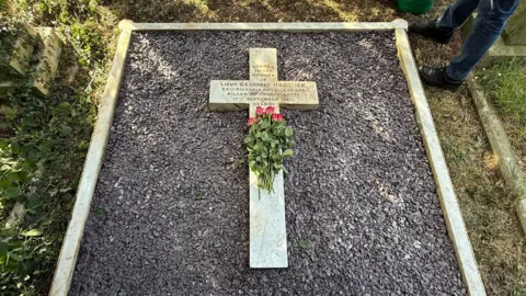 The grave of the first Titanic survivor, his and child. With a white marble cross and purple ceramic bits. 