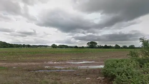 Google An area of muddy farm land, lined with trees 