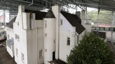 A large white building, with a protective roof and covering placed over the whole building
