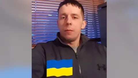 A man, Stefan Sivers, wearing a zip-up dark top and looking at the camera, with a Ukraine flag superimposed on the image.