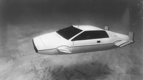Screen Archives/Getty Images El automóvil Lotus Esprit que aparece en la película de 1977 La espía que me amó. El coche blanco, con aletas que sobresalen a los lados y hélices en la parte trasera, flota bajo el agua cerca del fondo marino en esta imagen en blanco y negro.