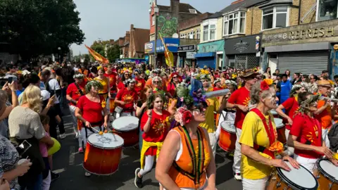 A street carnival with dozens of people dressed in bright colours
