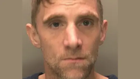 Head and shoulders police mugshot of John Arnold, who has a light-coloured beard and  is looking straight ahead 