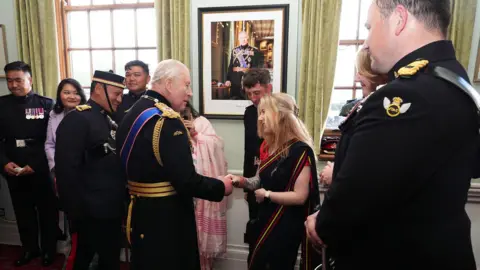 PA Media The King shakes hands with a woman. Other people are with them. He is indoors, dressed in ceremonial military uniform.