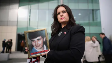 Getty Images Donna Miller holding a picture of her brother, Paul Carlile