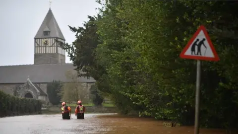 Getty Images Hereford Fire and Rescue personnel check the depth of flood water as they go along a flooded road in the village of Hampton Bishop in Herefordshire