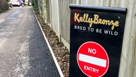 A black sign that says "KellyBronze, bred to be wild". Underneath the text is a red circle that says "no entry". The sign is at the bottom of a long driveway.