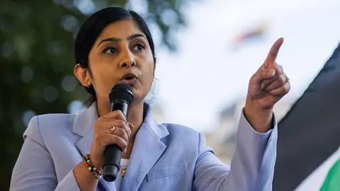 Getty Images Zarah Sultana, wearing a pale blue suit giving a speech with a microphone.