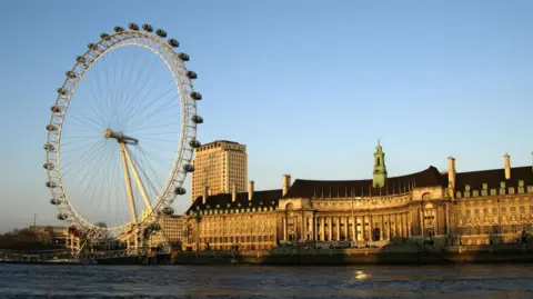 The London Eye in front of the former County Hall on the river Thames at sunset.