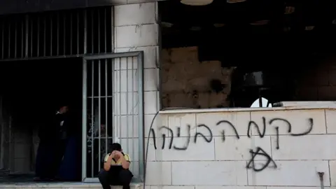 Reuters Un niño se sienta con la cara entre las manos frente a una mezquita dañada que tiene grafitis en sus paredes.