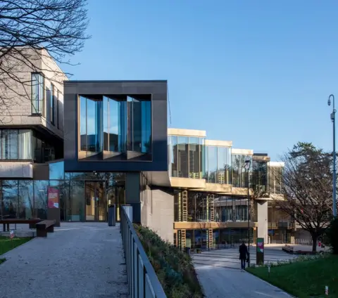 Paul Zanre Campus Central is a sandstone and glass building bordering a tree lined pedestrian plaza.