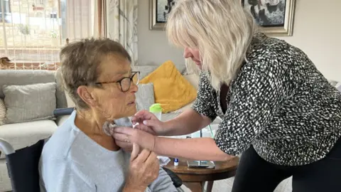  Shelley clearing Maureen's laryngectomy in a front room setting.