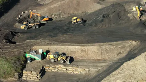 BBC A quarry site with several yellow excavation vehicles working on it 