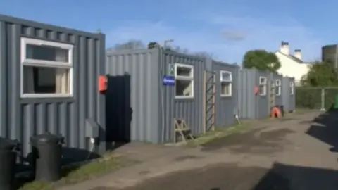 BBC Several grey corrugated iron temporary housing units.