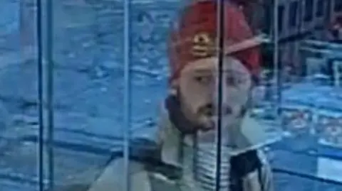 Metropolitan Police The man is shown behind a glass door looking past the camera wearing his red hat