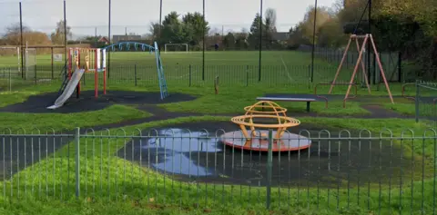 Google Dobree Park Playground with swings and a slide, surrounded by a fence