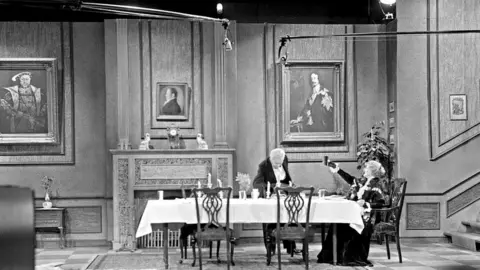 Alamy A wide shot of the Dinner for One production is seen here, with boom mics extending from the sides and the set dressing clearly visible.