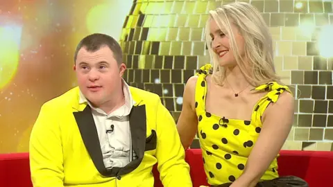 BBC Nathan Morris and his partner Jo Banham being interviewed by the BBC. They are both wearing yellow outfits