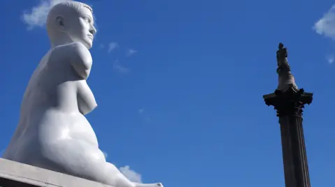 Getty Images Marble statue on a plinth alongside Nelson's Column with a blue sky