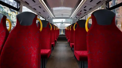 The inside of a bus which has red seats with yellow handles.
