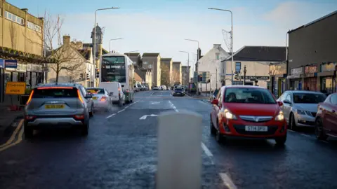 A street with shops on either side and cars going in both directions