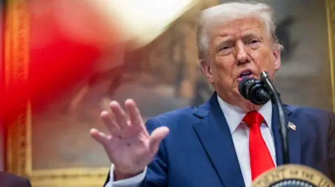 Getty Images Donald Trump speaking at a microphone wearing a blue suit and red tie