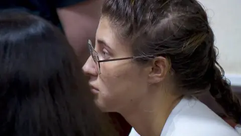 AP Bella Culley photographed in court from the side. She is wearing glasses and has brown hair in a plait and is wearing a white top