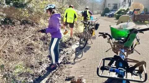 Stroud District Council Litter picking cyclists stopping to pick up rubbish with long grabbers from a verge