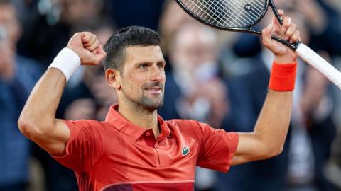 Novak Djokovic raises his arms and racquet in celebration