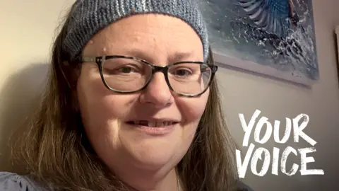 Selfie of Sarah Bodger, who has brown hair and is smiling at the camera. She is wearing a blue knitted hair band, glasses, and a blue top. The words "Your Voice" also appear in the bottom right corner of the picture.