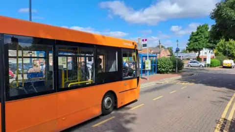 An orange bus pulls up at stop