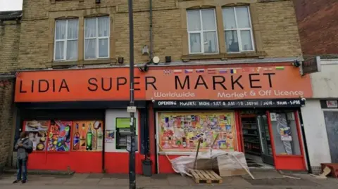 Lidia Supermarket on Sheffield Road in Barnsley which has been told to close for three months because it was selling illegal products. The shop has an orange sign with a pallet and rubbish outside. A man is standing on the left of the picture.