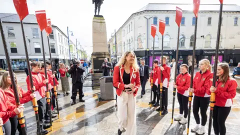 Causeway Coast and Glens Borough Council Members of Bann Rowing Club forming a guard of a Guard of Honour outside Coleraine Town Hall. They are wearing red coats and holding padels. Hannah Scoot is smiling as she walks down though the guard. 