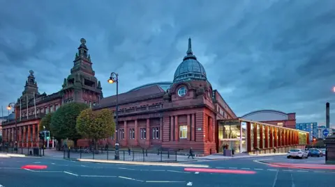 The Kelvin Hall - a red sandstone building in Glasgow. A modern glass annex is added onto the side of the historic building. 