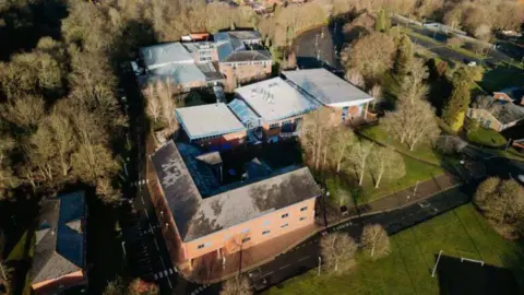 Telford & Wrekin Council An aerial view of a university campus, including six orange brick buildings with grey roofs. The buildings are surrounds by trees and a grey road.