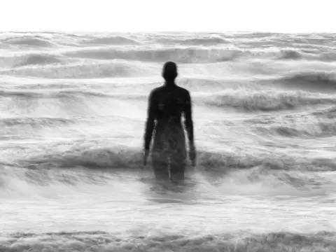 Sean Corlett A statue standing at sea while surfing on the beach