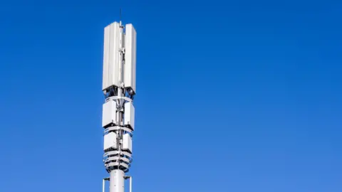 A tall post in the city with 5G mobile phone telecoms signal equipment against a clear blue sky.