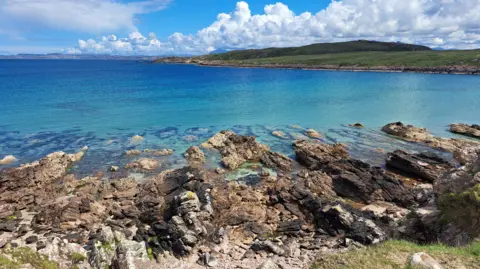 Gea Otten A sun-kissed view of a beach, sea and land in the distance