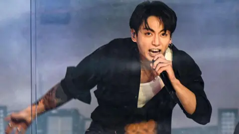 BTS vocalist Jungkook, in a black long-sleeved shirt, midway through a performance on stage