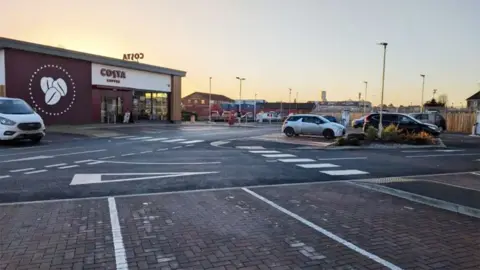 View of the Costa coffee car park with marked parking bays in the foreground and the single-storey store in the background