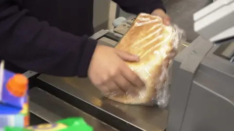 BBC A loaf of white bread is scanned in a supermarket till.