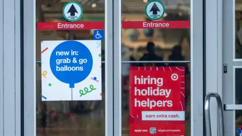 Bloomberg via Getty Images A red sign reading "Hiring Holiday Helpers" hangs on a glass entry door to a Target store.