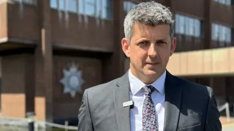 A head and shoulders image of Suffolk Police's detective inspector for the Joint Major Investigations Team, Dan Connick. He is wearing a suit and tie and looking directly into the camera.