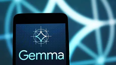 Getty Images Google's Gemma logo displayed on a smartphone, against a backdrop of an enlarged, blurred version of the same logo.