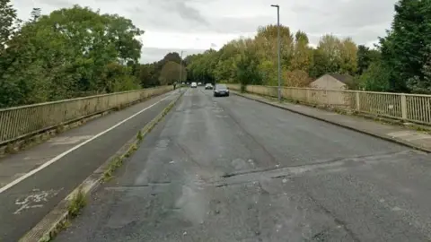 A Google Streetview screenshot of the viaduct on Eastern Way in Carlisle. The single-carriage road has a footpath on one side and a footpath and cycle lane on the other, with a metal parapet. 