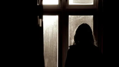 Silhouette of a woman looking out of a window. 