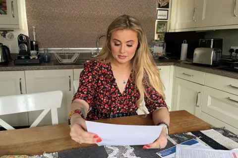 Rosey Hudson sits at a kitchen table and looks at one of the letters she received through the post